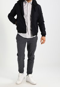 Granatowa kurtka na zamek z kołnierzem z kożucha, szara koszula na guziki oraz teksturowane ciemnoszare spodnie; do tego białe trampki.