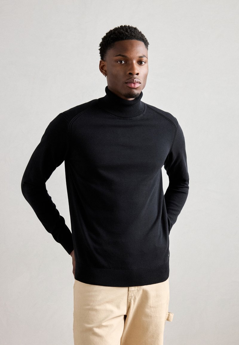Suéter negro de cuello alto hecho de una suave tela de punto, con puños y dobladillo acanalados, con una silueta ajustada y detalles de costura.