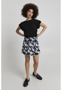 Sort kortærmet top med flæsedetaljer, parret med en marineblå blomsterskirt med hvide margueritter og sorte loafers.