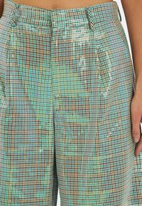Glinsterende geruite broeken in beige, groenblauw en aqua. Beschikt over een hoge taille, zijzakken en een gestructureerde pasvorm met sprankelende accenten.