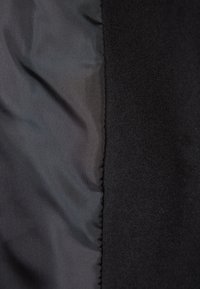 Svart tygpanel som visar två material: slät och glänsande till vänster och mjuk, texturerad fleece till höger, med en sammanfogad söm.