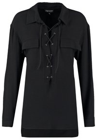 Chemise noire à manches longues avec col, devant à lacets et deux poches poitrine. Tissu doux avec une coupe décontractée.