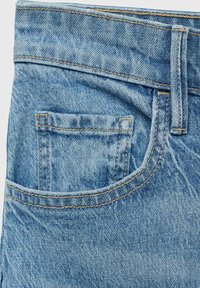Denim jeans med en lys blå farve og en falmet tekstur. Inkluderer en lille baglomme og kontrasterende syninger langs sømmene.