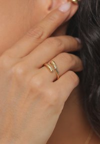 Guldplateret ring med et glat, buet design og to overlappende bånd. Overfladen er poleret, hvilket giver en reflekterende kvalitet.