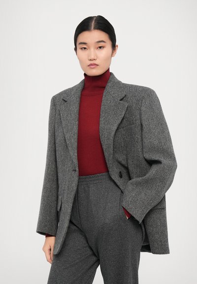 Grå herringbone-blazer med snibbkrage, kombinerat med en vinröd turtleneck. Texturerat tyg och avslappnade byxor fulländar looken.