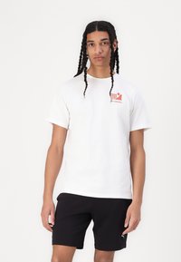 White cotton t-shirt featuring a red graphic design on the left chest area, paired with black shorts and a straight neckline.