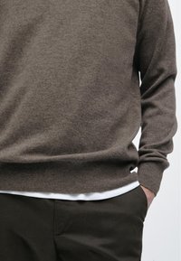 Brązowy wełniany sweter z okrągłym dekoltem, ściągaczami na mankietach i u dołu. Nosi się go na białej podkoszulce, w połączeniu z ciemnymi spodniami. Gładka tekstura.