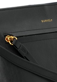 Borsa in pelle nera con superficie texturizzata, dotata di logo dorato, chiusura con zip e tracolla coordinata. Accentuata con dettagli metallici dorati.