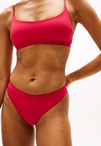 Red bikini set featuring a seamless bralette with thin straps and matching brief with a soft, stretchy texture and embossed logo detail.