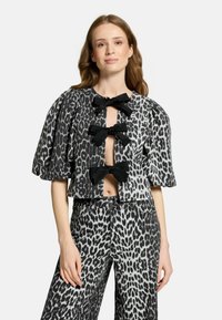 Top corto in stampa leopardata bianca e nera con maniche a sbuffo, dotato di tre grandi fiocchi neri e un design con frontale aperto. Abbinato a pantaloni coordinati.