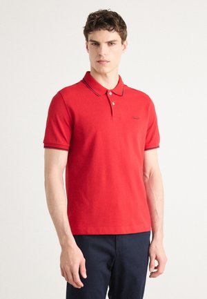 Camisa polo roja de algodón, con un cuello clásico, tapeta de dos botones y acentos en marino en las mangas y el cuello.