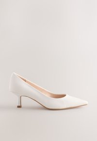 Hvid læderpumps med spids tå og lav, blokhæl. Glat tekstur og minimalistisk design med en neutral inderside.