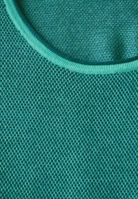 Texturerad teal-färgad tyg med rund halsringning och en kontrasterande ljusblå ribbad trim, som visar ett tätt stickat mönster och en jämn yta.