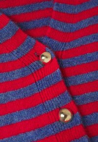 Cardigan a rayas rojas y azules en un suave punto, con un botón dorado redondo y una textura acanalada en los bordes.