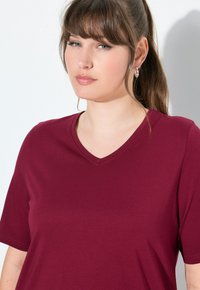 T-shirt bordeaux con scollo a V in morbido tessuto e maniche corte. Presenta dettagli di cucitura sottili; design semplice senza pattern o accenti.