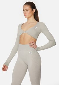 Helles graues Sportanzug-Set mit einem langärmeligen Crop-Top mit V-Ausschnitt und passenden hoch taillierten Leggings, beide mit dezenten Logo-Details.