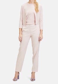 Světle růžový zkrácený kardigan přes laděný top a na míru šité kalhoty; charakterizován hladkou látkou a sandály s blokovým podpatkem v levandulové barvě.