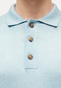 Γαλάζια πλεκτή πόλο μπλούζα με τρία καφέ κουμπιά, εμφανιζόμενη σε άτομο από τον λαιμό έως το στήθος.