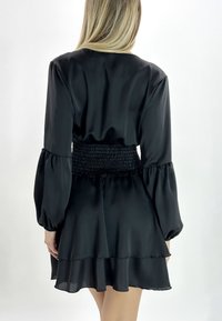 Zwarte jurk van gladde stof, met een smocktaille, pofmouwen en gelaagde ruches aan de zoom.