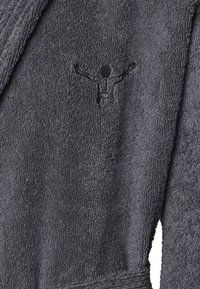 Grauer Bademantel aus Frottee mit strukturiertem Oberflächen; mit einem in Schwarz gestickten Logo und einer stilisierten Figur. Saugfähiger Stoff, mittellanges Design.