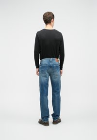 Ανδρική εμφάνιση με μαύρη μακρυμάνικη μπλούζα και ξεθωριασμένα μπλε τζιν παντελόνια, τα οποία διαθέτουν καφέ δερμάτινη ετικέτα στη ζώνη και δύο πίσω τσέπες.