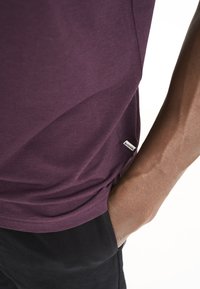 Lilla kortærmet T-shirt i et blødt materiale, med et lille mærke på kanten. T-shirten har en afslappet pasform og en glat overflade.
