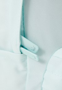 Närbild av ljusblått tyg med två Adidas-märkta dragkedjeskydd fästa vid en väska eller ryggsäck.