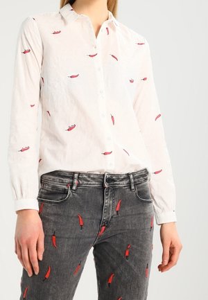 White button-up shirt and gray jeans both patterned with small red chili peppers, worn by a person from neck to hips.