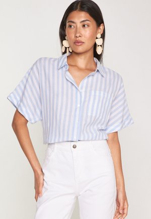 Lichtblauw en wit gestreept kortemouwen shirt met knoopsluiting aan de voorkant en zak; gecombineerd met witte hoge taille broek.