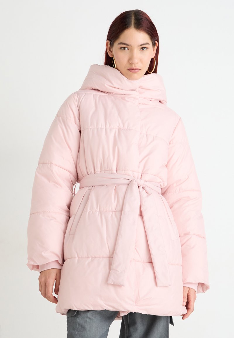 Polstret rosa frakk med belte i livet, høy krage og sidelommer. Har et quiltet design og myk, glatt tekstur.