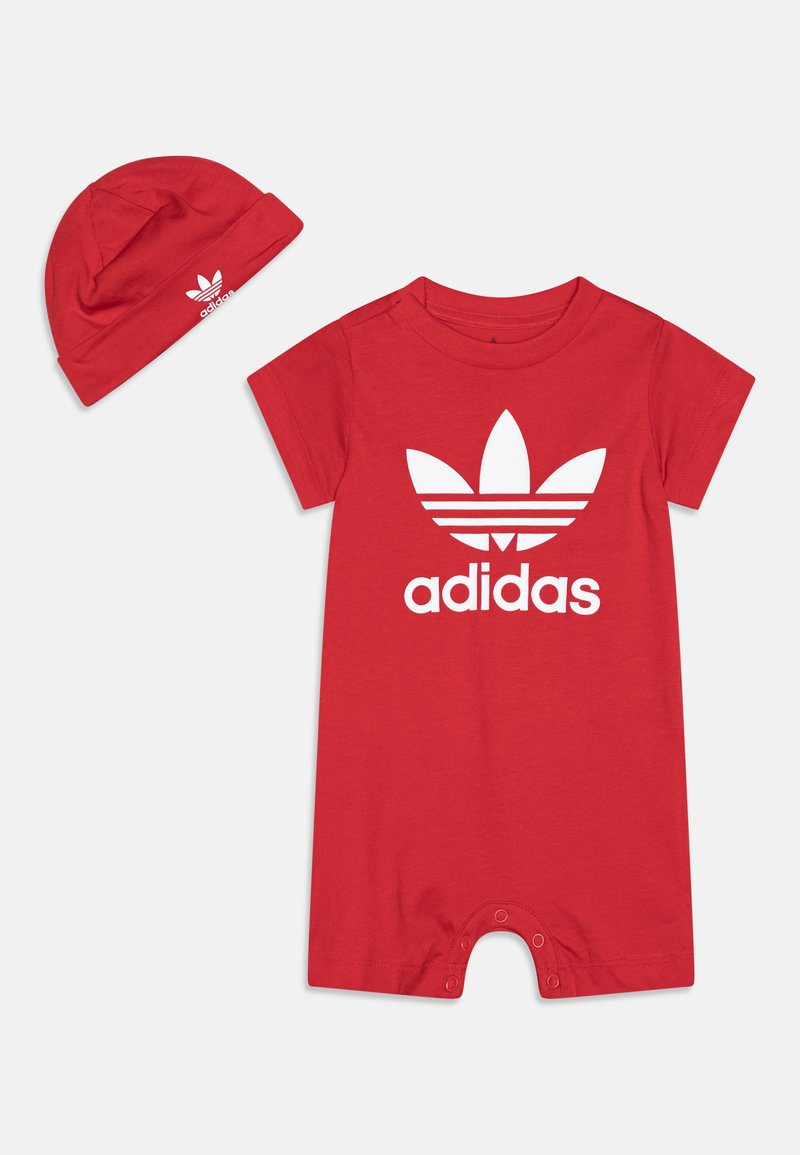 Sarkans kokvilnas romperis ar īsām piedurknēm, kas rotāts ar lielu baltu Adidas logo un trīs svītru dizainu. Komplektā ietilpst arī atbilstoša sarkana cepure.
