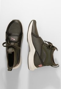 Dark green athletic shoes with mesh accents, textured fabric, white soles, and pink logo detailing. Rounded toe and lace-up design.