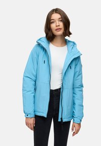 Giacca a vento azzurro chiaro con cappuccio, zip frontale, dettagli con stringa e polsini elasticizzati; abbinata a un top bianco e pantaloni neri.