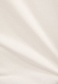 Gros plan sur un tissu côtelé doux de couleur crème avec de fines lignes verticales et de légers plis créant des ombres texturées.