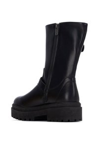Botas de tobillo de cuero negro con cremallera lateral, suela gruesa negra y un acabado suave. Presentan un detalle de correa alrededor del tobillo.