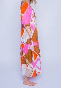 Pitkä, väljä mekko, joka on valmistettu kevyestä kankaasta. Ominaisuuksiin kuuluu rohkeita geometrisia kuvioita vaaleanpunaisessa, oranssissa, ruskeassa ja valkoisessa. Sisältää sivutaskut.