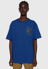 Blaues Baumwoll-T-Shirt mit kurzen Ärmeln und Rundhalsausschnitt. Verfügt über einen grafischen Aufdruck auf der Vorderseite mit verschiedenen Textelementen und einem quadratischen Design.