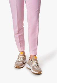Sneakers with a mesh upper, beige and taupe accents, white sole, and textured detailing. Paired with light pink tailored pants.