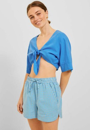 Top corto azul con lazo en el frontal, con mangas cortas. Combinado con pantalones cortos de cuadros azul y blanco, cintura elástica con cordón.