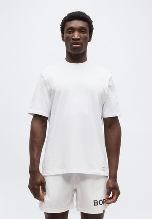 Mand iført almindelig hvid oversized t-shirt og hvide shorts med teksten "BORG", stående mod en ensartet lys baggrund.