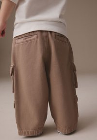 Bruine cargoshorts met zijzakken, gemaakt van duurzaam materiaal. Heeft een ontspannen pasvorm en zichtbare stiksels aan de tailleband en zakken.