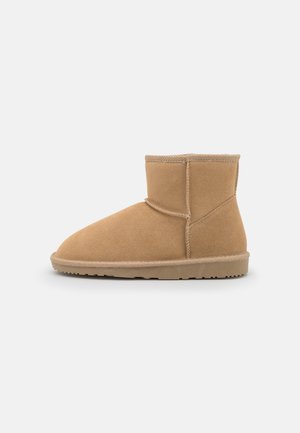 Bottine courte en daim beige avec semelle plate et coutures visibles sur les côtés, conçue pour une tenue décontractée.