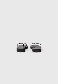 Schwarze Flip-Flops mit strukturiertem Fußbett, ausgestattet mit einer dicken Sohle und minimalistischem Riemendesign, von hinten betrachtet.