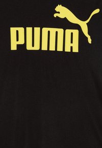 Svart t-shirt med stor gul "PUMA" text och en hoppande puma-logotyp, tillverkad av mjuk bomullstyg. Minimalistisk design med djärva färger.