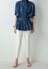 Marinblå lätt skjorta med smockad midja, korta ärmar och hög krage, i kombination med vita skräddarsydda byxor och nude-hälar.