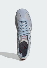 Light blue sneaker with suede and mesh panels, featuring grey stripes, textured interior, and a red logo on the insole.