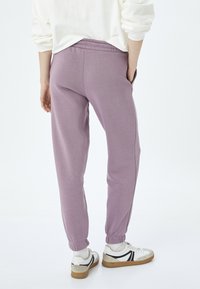 Lyslilla sweatpants med elastisk talje og manchetter, med sidelommer. Sammen med hvide sneakers og hvide strømper.