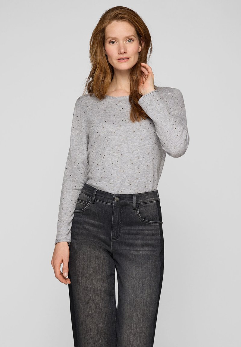Graues Langarmshirt mit rundem Ausschnitt und kleinen metallischen Akzenten, kombiniert mit dunklen, hoch taillierten Jeans aus Denim. Glatte Textur.