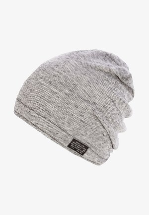Bonnet en tricot gris clair, ample, avec une petite étiquette en tissu noir cousue sur le bord.