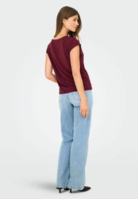 Top corto burdeos de manga corta con un corte relajado, combinado con unos jeans de tiro alto de color azul claro y unos tacones negros con punta. Diseño sencillo, textura suave.